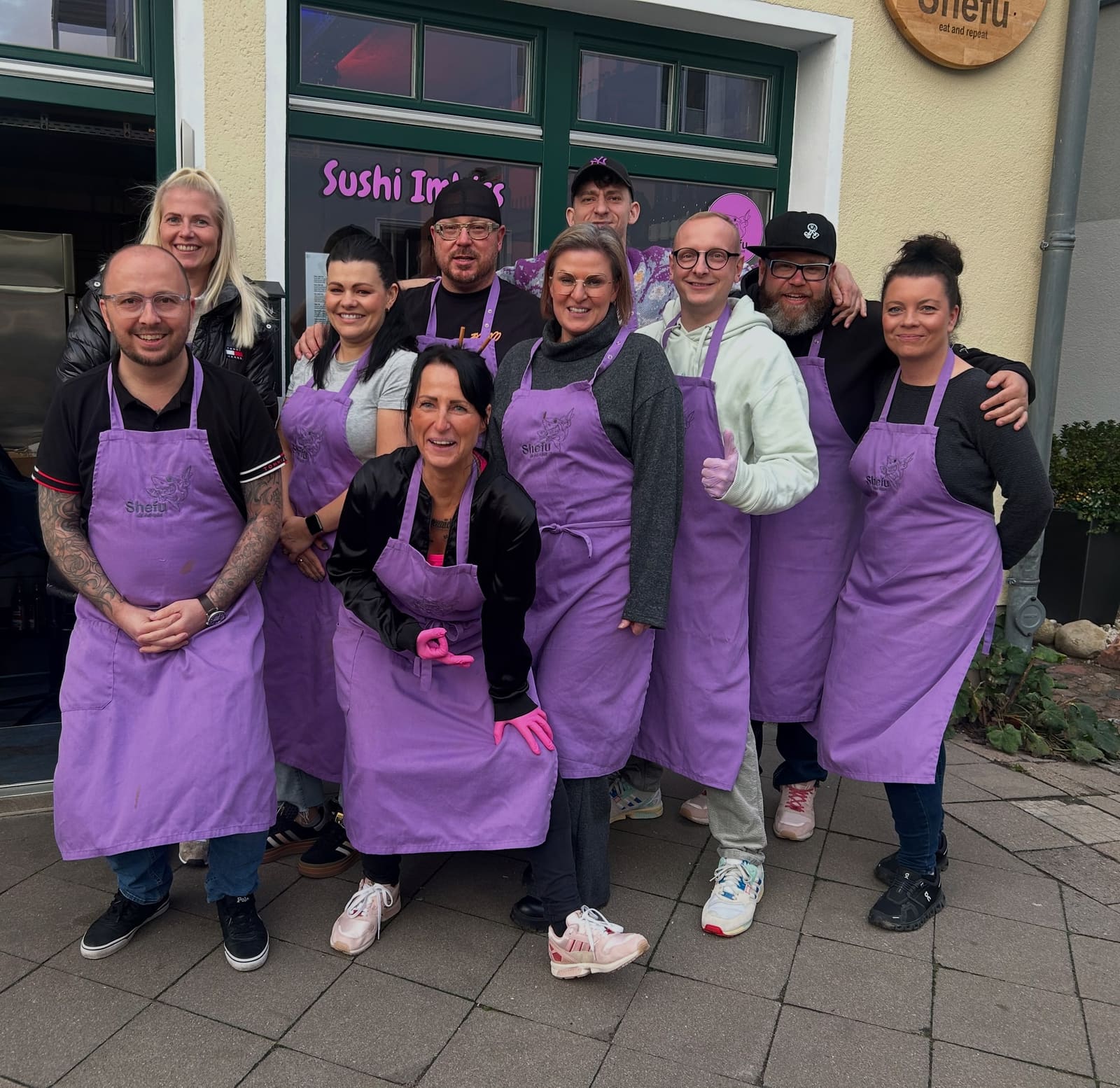 Workshop-Gruppe in lila Shefu-Schürzen vor dem Sushi-Imbiss in Warnemünde